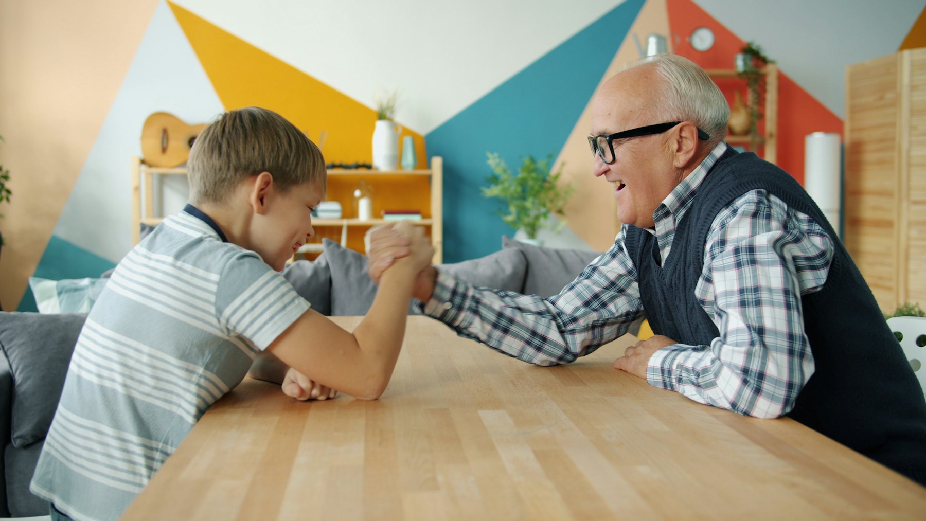 A grandfather and grandson arm wrestling at a table, both laughing